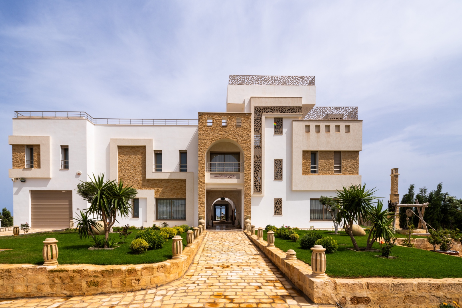 Dar Aïcha à Tazarka — façade contemporaine tunisienne avec allée d'accès et jardin méditerranéen